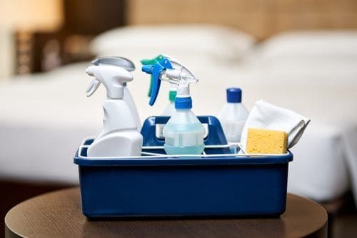 Cleaning supplies caddy on a freshly made bed during a vacation rental turnover clean