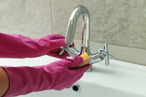 Cleaner in pink gloves scrubbing a kitchen faucet to remove hard water scale