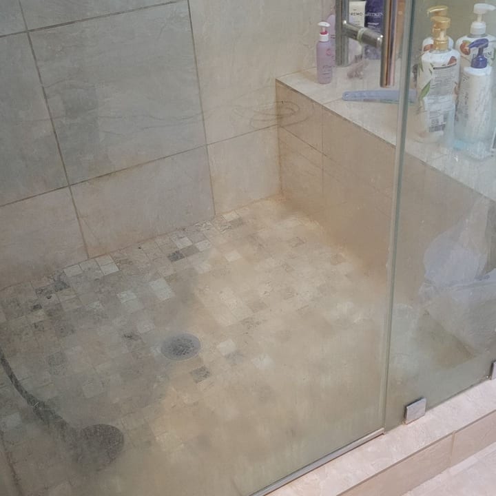 The same glass walk-in shower before cleaning, with soap scum on the glass and tile