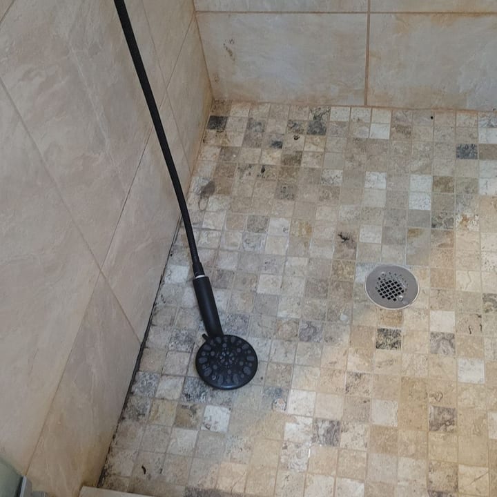 Mosaic-tile shower floor before cleaning, with grime around the drain