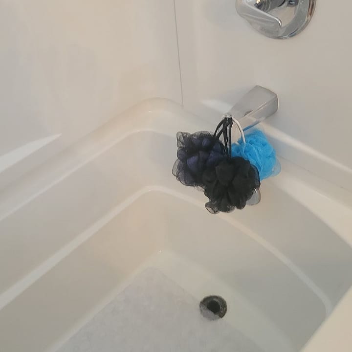 White bathtub after scrubbing, with a loofah on the faucet