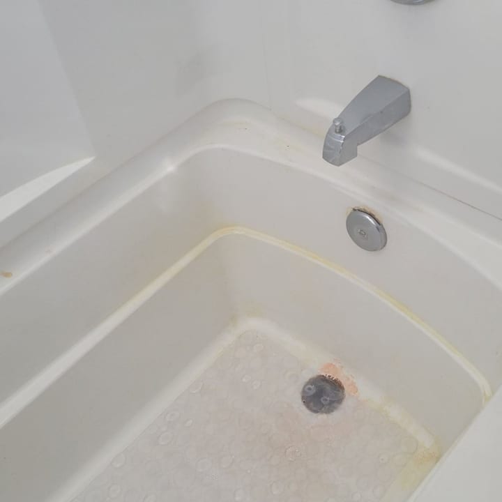 The same bathtub before cleaning, with a grime ring and stained surround
